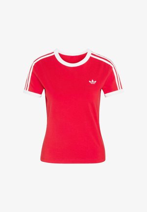 Czerwona bawełniana koszulka z białym prążkowanym dekoltem i mankietami. Na każdym ramieniu znajdują się trzy białe paski oraz małe białe logo na piersi.