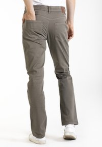 Pantalons en coton gris avec une coupe droite, comportant deux poches arrière et une étiquette en cuir de marque au-dessus de la ceinture. Baskets blanches visibles.