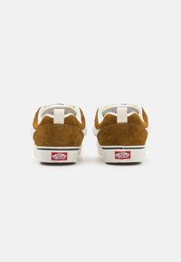 Brune semskede sneakers med en hvid læderbund, der har en forstærket hæl, polstret krave og "Vans Off the Wall" logo på hælen.