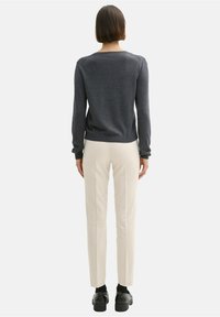 Dunkelgrauer Strickpullover mit langen Ärmeln, kombiniert mit cremefarbenen gerade geschnittenen Hosen und schwarzen Schuhen, von hinten gesehen.