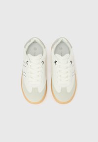 Ζευγάρι λευκών και μπεζ αθλητικών παπουτσιών με καουτσούκ σόλες και λευκά κορδόνια, φωτογραφημένα από πάνω σε λευκό φόντο.