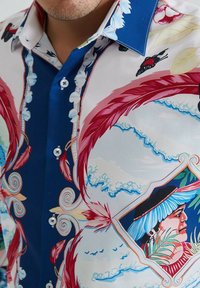 Chemise à manches courtes avec un motif abstrait coloré comprenant des plumes rouges, un fond bleu et un portrait dans un cadre décoratif.