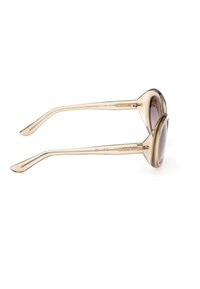 Lunettes de soleil beiges translucides en forme d'œil de chat avec des verres foncés et le logo "GUESS" sur les branches, présentées de profil sur un fond blanc.