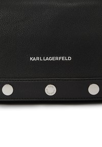 Borsa in pelle nera con superficie testurizzata, hardware in tono argento e marchio stampato. Dettagli notevoli includono borchie circolari.
