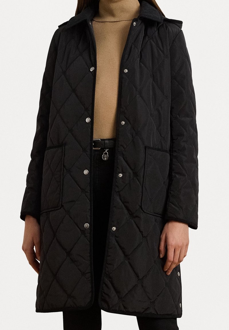 Svart vadderad kappa med tryckknappar, två framfickor och en krage. Tyget är slätt med ett mönster av texturerade diamanter.