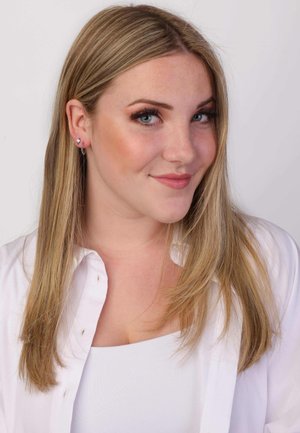 Blond haar met een subtiele golf, draagt zilveren runwayringen en een witte blouse over een witte top, tegen een effen achtergrond.