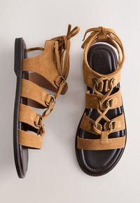 Sandales gladiateur en daim marron à lacets, avec plusieurs lanières et semelles noires rembourrées, vues de dessus et de côté.