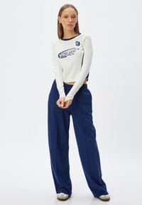 White long-sleeve crop top with navy accents and printed text, paired with loose-fitting navy pants. Features a relaxed design.