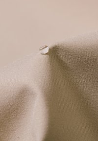 Beiger strukturiert Stoff mit einem Wassertropfen, der auf einer Falte ruht, was die Glätte und die wasserabweisenden Eigenschaften des Materials zeigt.