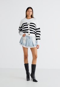 Black and white striped cardigan, button-up front, ribbed material. Paired with a light blue pleated denim skirt and black heeled boots.