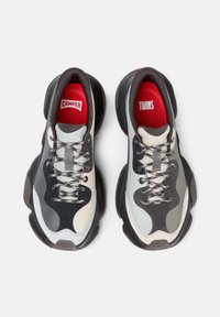 Sneakers robusti con un upper in nero, grigio e crema, realizzato in materiali scamosciati e in mesh. Presentano lacci metallici e solette brandizzate rosse.