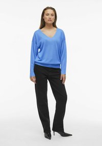 Modra v-neck pulover, ohlapen kroj, dolgi rokavi. V kombinaciji z črnimi naravnost krojenimi hlačami in črnimi čevlji s špičastim nosom. Gladka tekstura.
