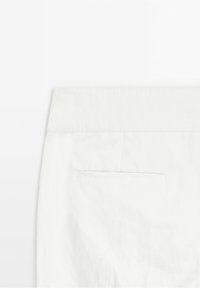 Pantalon blanc montrant la partie haute du dos avec une ceinture et une poche passepoil horizontale unique.