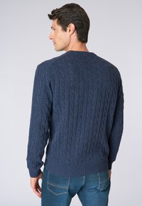 Maglioncino blu a maglia intrecciata con polsini e orlo a coste. Presenta un collo a giro e un motivo testurizzato. Indossato con jeans blu.