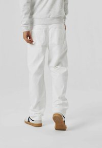 Pantaloni in denim bianco con vestibilità rilassata, dotati di tasche posteriori, indossati con un felpa grigia e sneakers bianco e nere. Tessuto strutturato.
