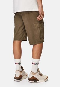 Bruna cargoshorts med sidofickor, matchade med vita strumpor med röda och gröna ränder, samt beige sneakers med bruna detaljer.