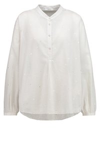 Blouse blanche à manches longues avec des petits points scintillants subtils, col rond, patte boutonnée et poignets légèrement froncés.