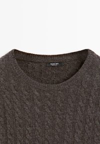 Maglione marrone a trecce con collo rotondo e bordi a coste. Il tessuto appare morbido e strutturato, con un delicato design di motivi intrecciati.