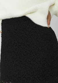 Jupe texturée noire avec une silhouette légèrement évasée. Confectionnée dans un tissu tissé, présentant un motif floral et un ourlet subtilement transparent.