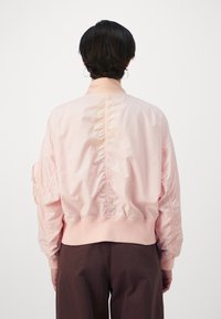 Pink bomber jacket with a smooth, shiny texture, gathered back, ribbed cuffs, and waistband. Features dropped shoulders and oversized fit.