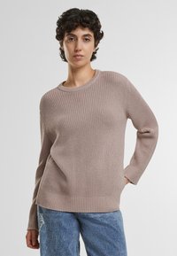 Lyserød strikket sweater med ribbet tekstur, rund halsudskæring og lange ærmer. Kombineret med slidte blå denimjeans.