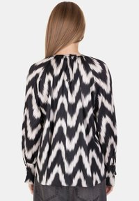Blusa a maniche lunghe con motivo a zig zag in bianco e nero, caratterizzata da un colletto posteriore arricciato e polsini con bottoni, realizzata in tessuto liscio.