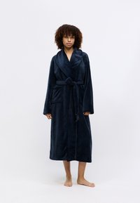 Navy sininen pehmeä kylpytakki, jossa on shaala-kaulus, pitkät hihat ja sidottava vyötärö. Takissa on kaksi etutaskua ja pehmeä rakenne.