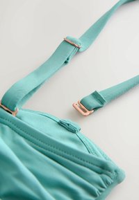 Türkizkék melltartó állítható pántokkal, rózsaarany színű fém díszítéssel. Sima textúrájú, varrással és kampós kapoccsal.