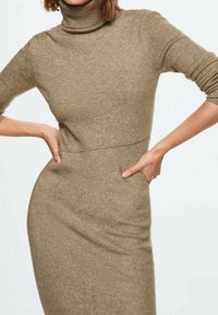 Vestido de cuello alto de punto en marrón claro. Diseño ajustado con mangas tres cuartos y una textura suave y lisa. Detalles de costura mínimos.