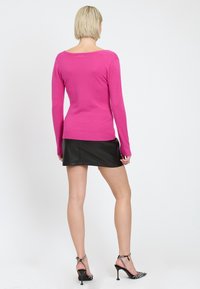Top lungo a maniche di colore rosa brillante con scollo rotondo, abbinato a una mini gonna nera in ecopelle. Presenta un design aderente e dettagli con polsini a coste.