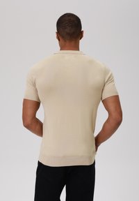 Kurzärmliges Poloshirt in Beige, mit gerippter Textur und tailliertem Design. Es hat einen klassischen Kragen und einen leicht abgerundeten Saum.