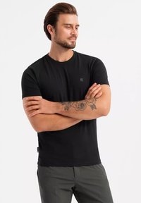 Czarny t-shirt z krótkim rękawem wykonany z bawełny, z okrągłym dekoltem, z małym logo na piersi i gładką, jednolitą fakturą.