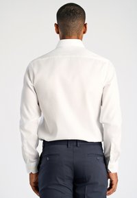 Camicia bianca a maniche lunghe con colletto classico, texture liscia e bottoni sui polsini, abbinata a pantaloni sartoriali blu scuro.