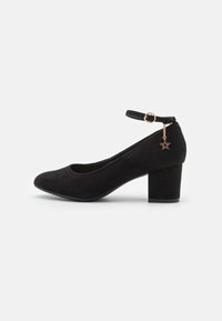Zapato de tacón de ante negro con correa al tobillo, puntera redonda, tacón grueso y detalle de charm en forma de estrella dorada en la correa del tobillo.