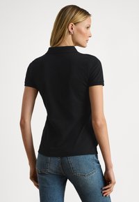 Svart poloshirt med korte ermer, tettsittende silhuett og klassisk krage, kombinert med blå jeans. Glatt stoff og minimalistisk design.