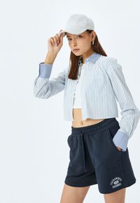 Korte, wit en blauw gestreepte blouse met puffed mouwen en marineblauwe shorts met een witte tekstlogo. Pet voegt een casual uitstraling toe.