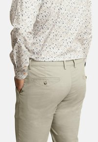 Pantalones verde claro con bolsillos traseros y detalles de botones, combinados con una camisa color crema con un patrón floral en azul y marrón.