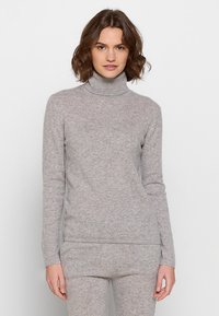 Grau gestrickter Rollkragenpullover aus weichem, strukturiertem Material. Figurbetontes Design mit langen Ärmeln und geripptem Kragen, kombiniert mit passenden Hosen.