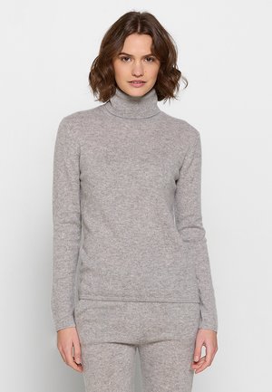 Šedý rolák vyrobený z jemné, strukturované pleteniny. Upnutý design s dlouhými rukávy a žebrovaným límcem, nošený s ladícími kalhotami.