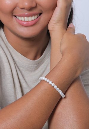 White pearl bracelet on a wrist, featuring round pearls of uniform size, set on a flexible thread, worn against a neutral skin tone.