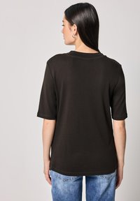 T-shirt in cotone nero con maniche corte, scollo rotondo e vestibilità rilassata. Il retro presenta una semplice cucitura e un orlo leggermente curvo.