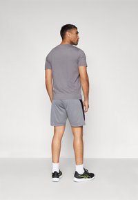 Grijze crewneck t-shirt gecombineerd met grijze shorts met zwarte zijaccenten. Model staat zijwaarts en draagt zwarte sportschoenen met groene details.