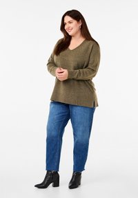 Olijfgroen gebreid sweater met een V-hals en geribbelde manchetten, gecombineerd met blauwe rechte jeans en zwarte enkellaarsjes met hak.