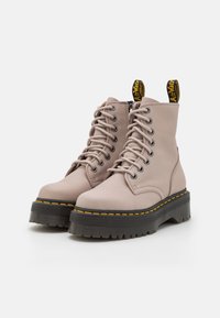 Botas de cuero rosa hasta el tobillo con una suela negra gruesa, costuras amarillas y diseño de cordones. Presenta un tirador de tela en el talón.