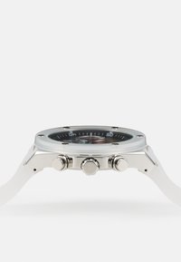 Reloj de pulsera cronógrafo plateado con una esfera negra redonda, acentos de acero inoxidable, tres botones de presión y una correa de silicona blanca.