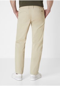 Beige chinos with a straight leg fit, made of smooth fabric. Features two back pockets and worn with white sneakers.