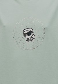 Ανοιχτό πράσινο μπλουζάκι με κεντρικό σχέδιο ενός κινούμενου χαρακτήρα με γυαλιά ηλίου, διακοσμημένο με στρας σε κυκλικό μοτίβο.