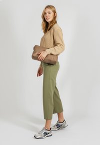 Beige csíkos pulóver, olajzöld cropped nadrág, ezüst torna cipő, és egy barna clutch táska. Egyszerű dizájn, texturált anyagokkal.