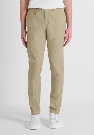 Pantalones beige de tela ligera, con un corte ajustado y bolsillos frontales. Combinados con zapatillas blancas.