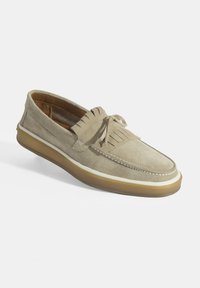 Beige suède instappers met een ronde neus, franjerdetails, witte stiksels en een lichtbruine rubberen zool. Overal een soepele textuur.